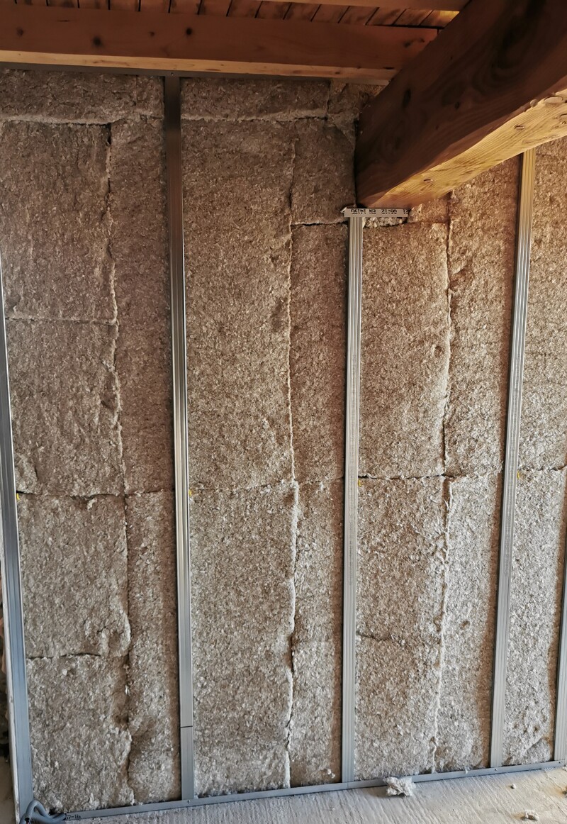 Isolation Murale Laine Minérale et Ossature Métallique Isolation thermique en laine minérale entre montants métalliques pour cloison, avec poutre en bois visible en haut. Texte visible sur montant : 06.12 21.00.